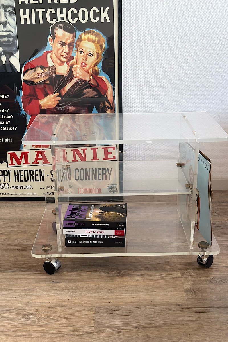 vue de face d'une table en plexiglas, avec des livres dedans . a l'arrière plan une affiche de cinéma