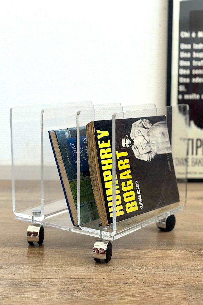 Porte-revues design en plexiglas transparent sur roulettes, marque Marais International, contenant un magazine