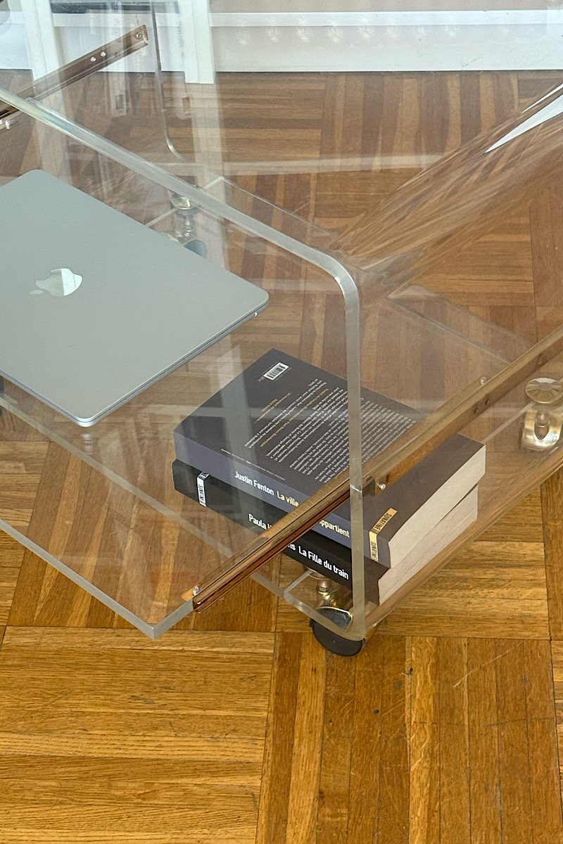 Gros plan sur l'angle supérieur d'une desserte en plexiglas transparent, montrant la finition arrondie du plateau et la tablette coulissante