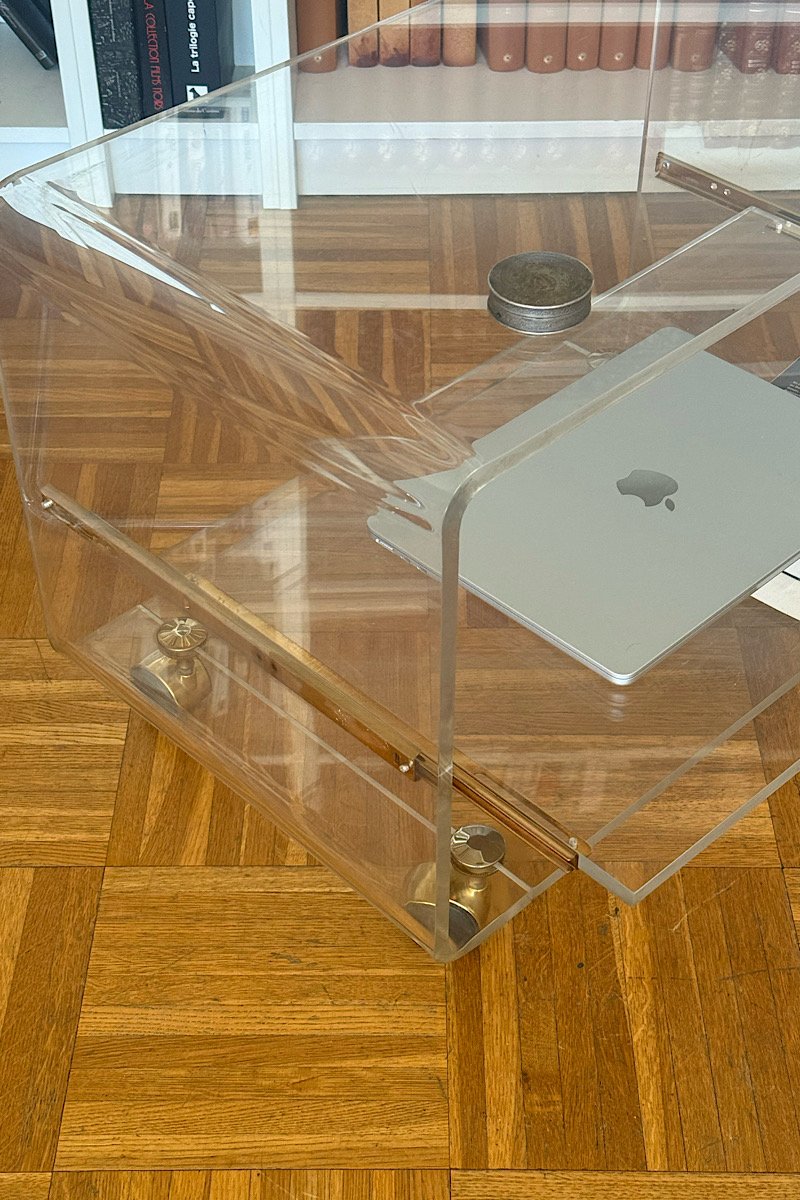 Gros plan en contre-plongée d'une desserte en plexiglas, soulignant la transparence des plateaux et les fixations métalliques sur un sol en parquet