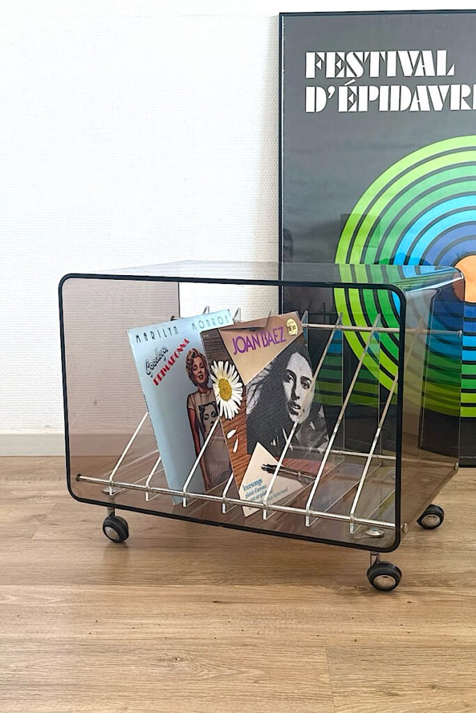 Vue de trois-quarts d'un range-vinyles en plexiglas transparent sur roulettes, laissant apparaître sa structure et les disques rangés à l'intérieur.