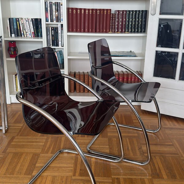 Vue de profil de deux chaises design "Blooming" créées par Yves Christin, mettant en valeur leur structure métallique tubulaire et leur assise élégante en plexiglas fumé.