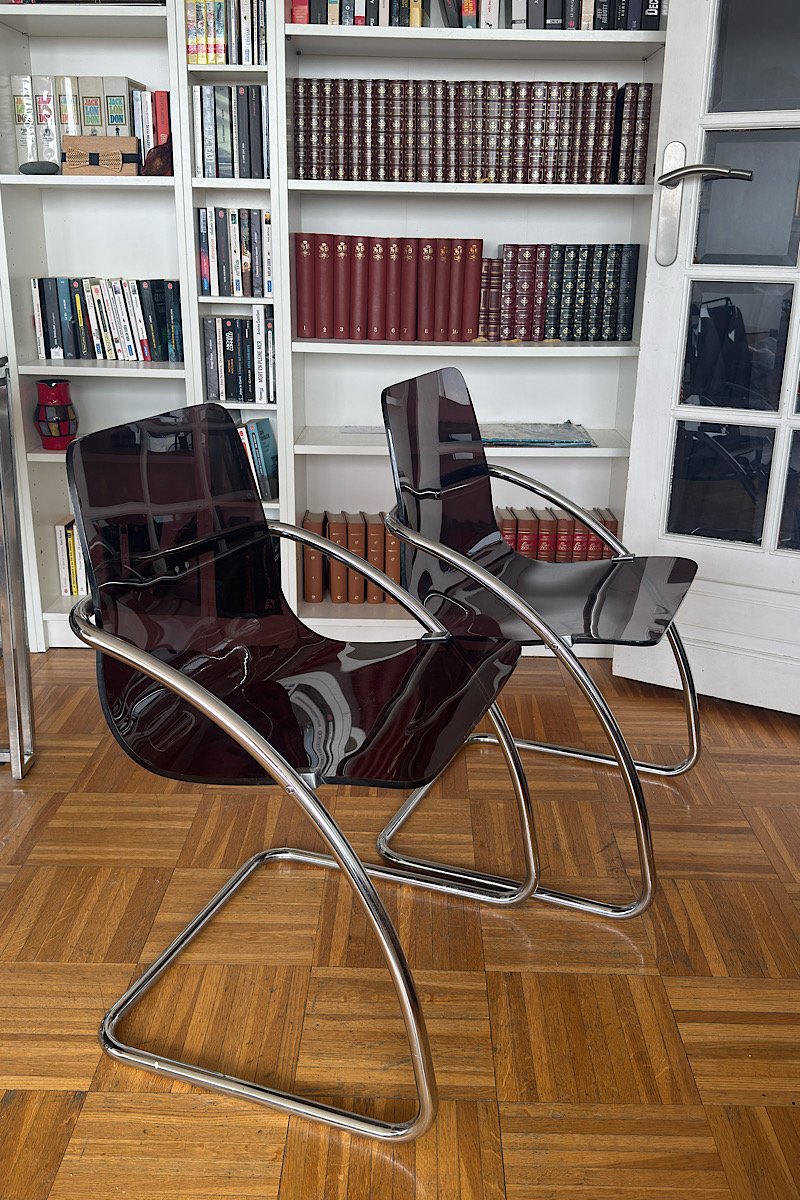 Vue de profil de deux chaises design "Blooming" créées par Yves Christin, mettant en valeur leur structure métallique tubulaire et leur assise élégante en plexiglas fumé.