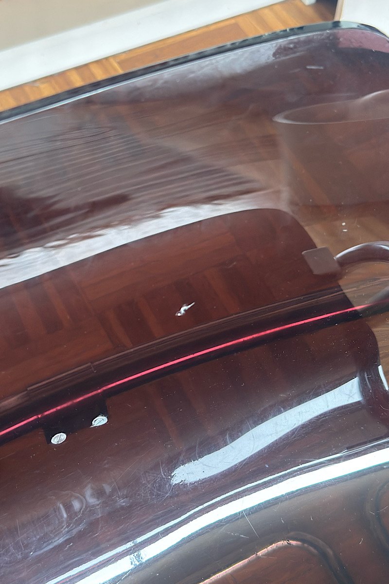 Vue détaillée d'un éclat dans le dossier d'une chaise design "Blooming" créées par Yves Christin, mettant en évidence leur structure métallique tubulaire et leur assise en plexiglas fumé dans un intérieur avec bibliothèque.