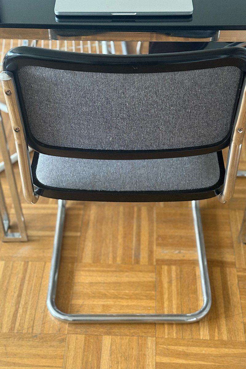 Vue de dos d'une chaise Cesca B32 de Marcel Breuer montrant l'arrière du dossier en tissu gris, le piètement luge en acier et le parquet