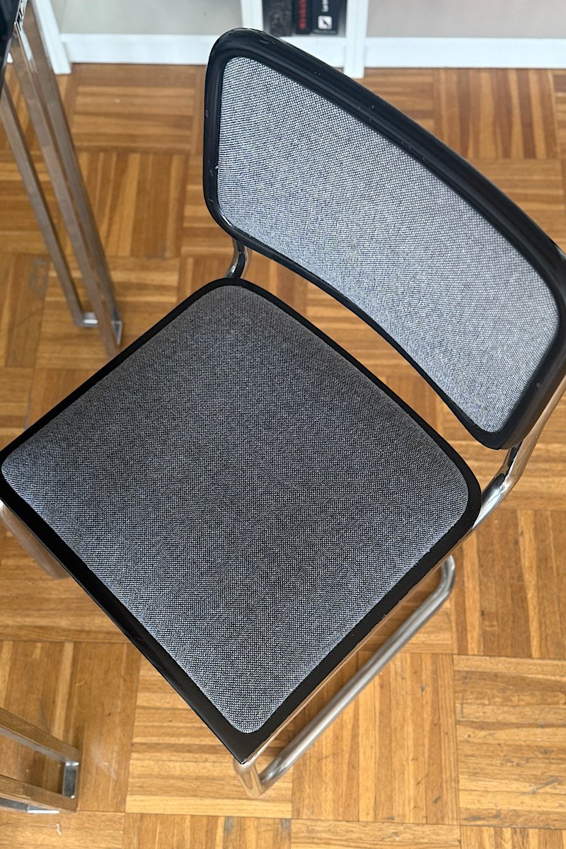 Vue en plongée sur l'assise et le dossier en tissu gris d'une chaise Cesca B32 de Marcel Breuer sur fond de parquet