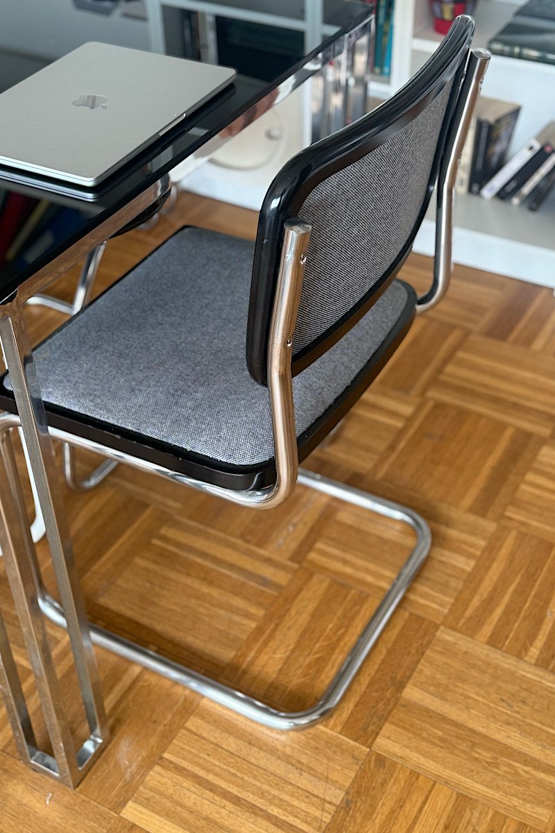 Vue de trois quarts arrière d'une chaise Cesca B32 de Marcel Breuer avec assise et dossier gris, placée à côté d'un bureau